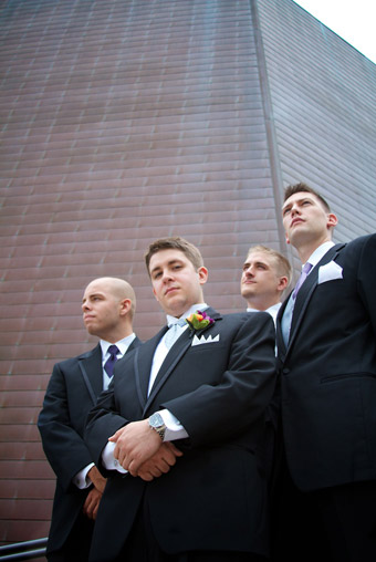 Upward look at groomsmen in cool pose in front of retro wall