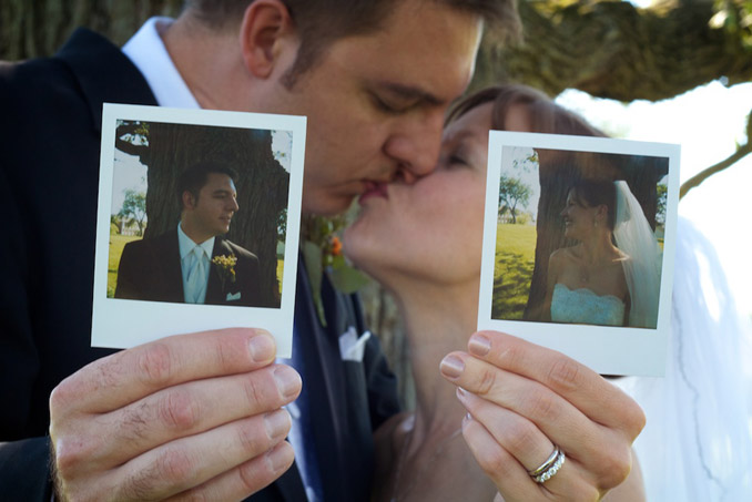 Bride and groom holding polaroids of themselves while kissing out of focus