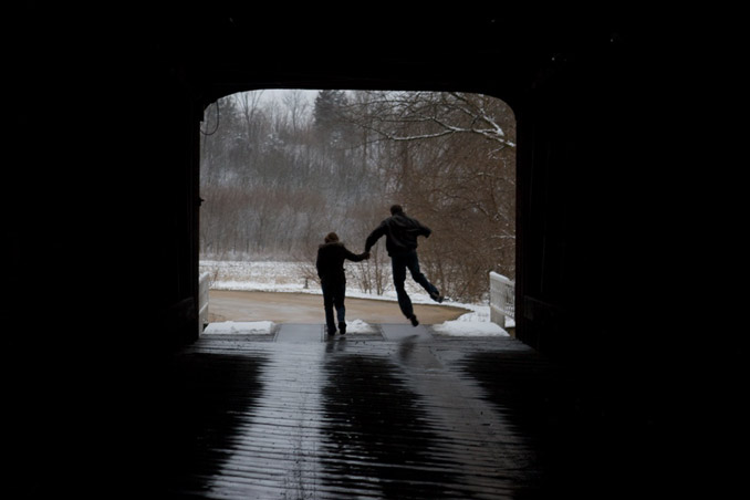 Silhouette of couple in opening of a covered bridge. Man is kicking his heels.