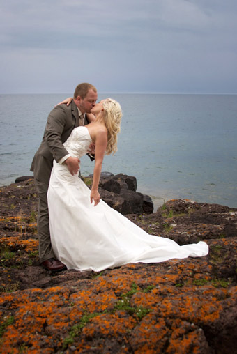 Wedding couple dipping to kiss on rocky shoreline of Lake Superior