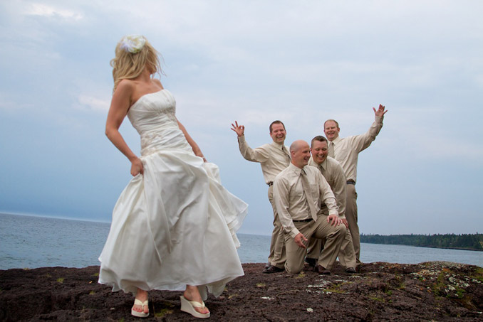 Bride looking back over shoulder at groomsmen on rocky coastline of Lake Superior